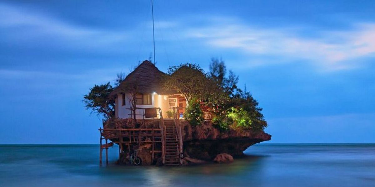 A coral rock in the ocean with a resturant ontop of it at night