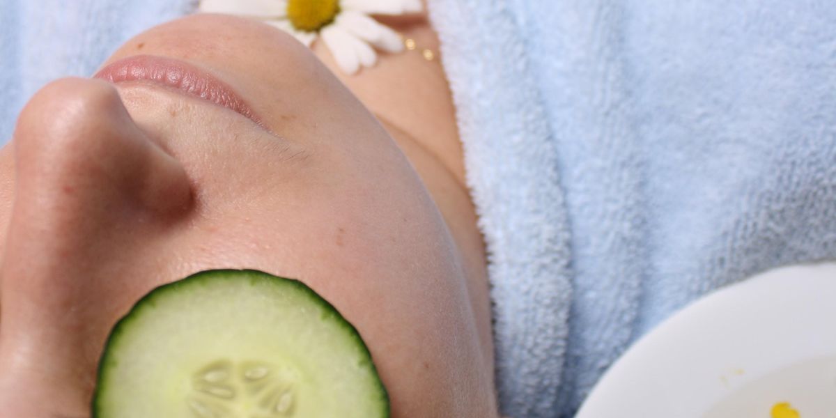 woman wearing blue robe lying with cucumber on eye